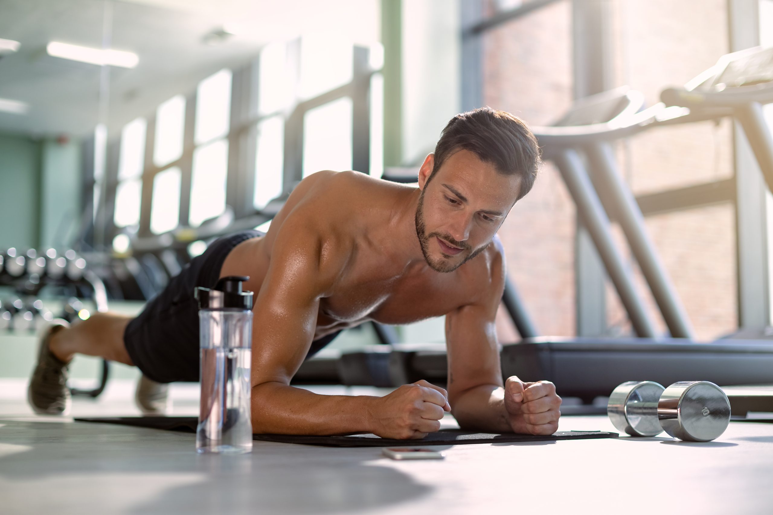 Muscular build athlete exercising in plank pose during cross training at health club.